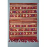 An ethnic hand-woven fringed scarf, decorated in a banded pattern on a red ground, 46 cm x 130 cm