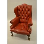 Pair of red button leather upholstered wing back armchairs raised on low cabriole claw and ball