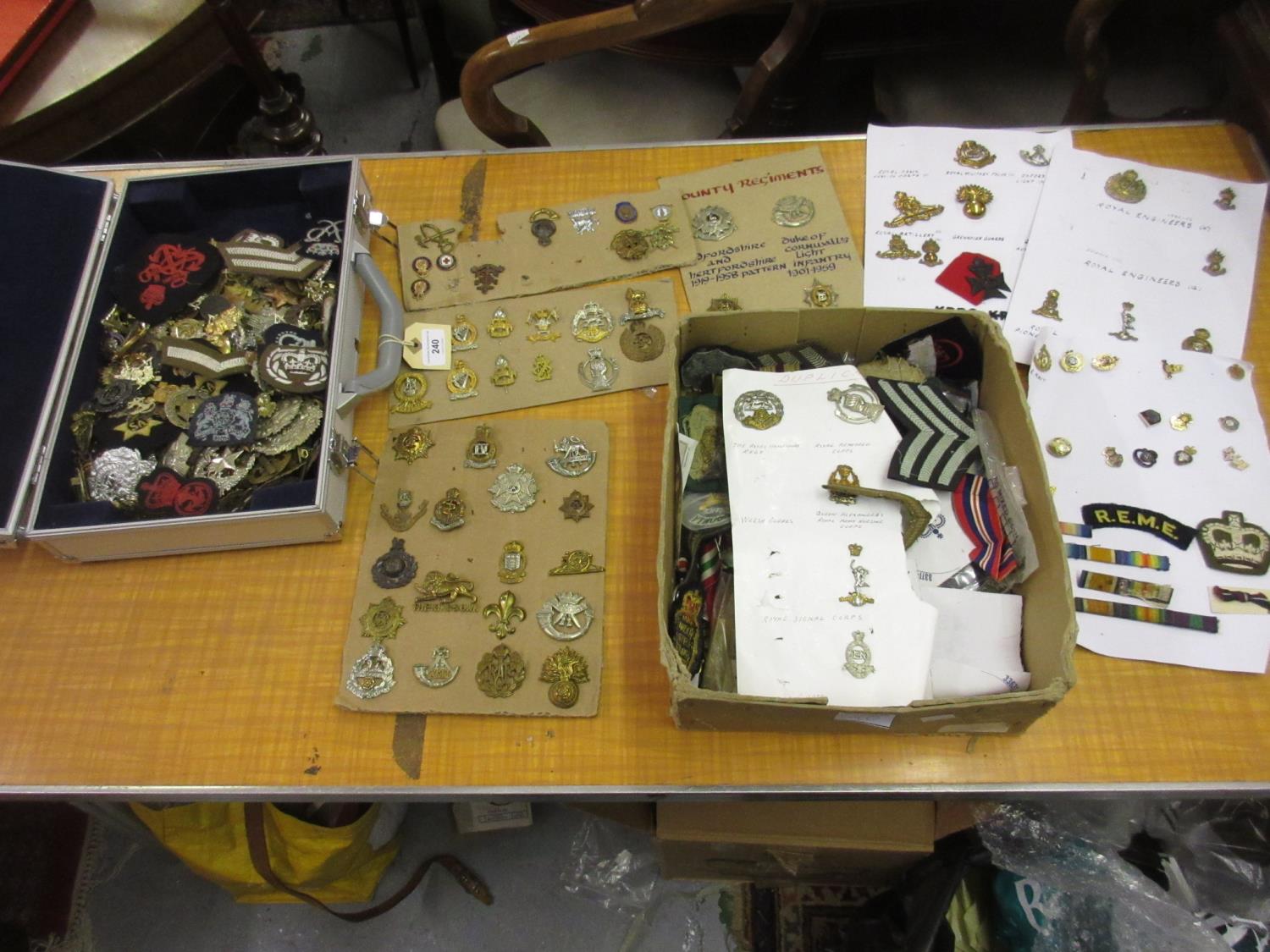 Box and silver case containing a large collection of over three hundred military cap badges, cloth