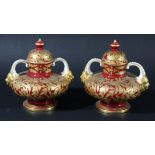 PAIR OF ROYAL CROWN DERBY LIDDED URNS each with gilded birds and leaves on a rich red ground,