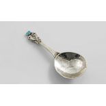 AN EDWARDIAN HAND-MADE SPOON with a hammered bowl, and a short stem, terminating in two cast