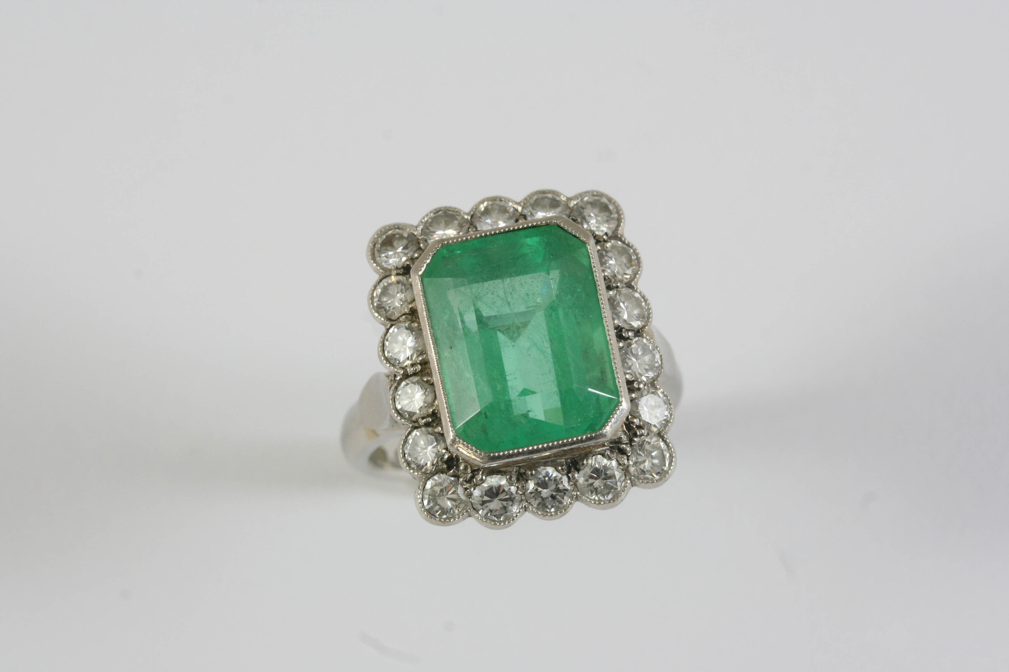 AN EMERALD AND DIAMOND CLUSTER RING the cut cornered rectangular shaped emerald weighs 8.10 carats