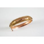 AN EARLY 20TH CENTURY GOLD, RUBY AND DIAMOND HALF HINGED BANGLE mounted to one side with three