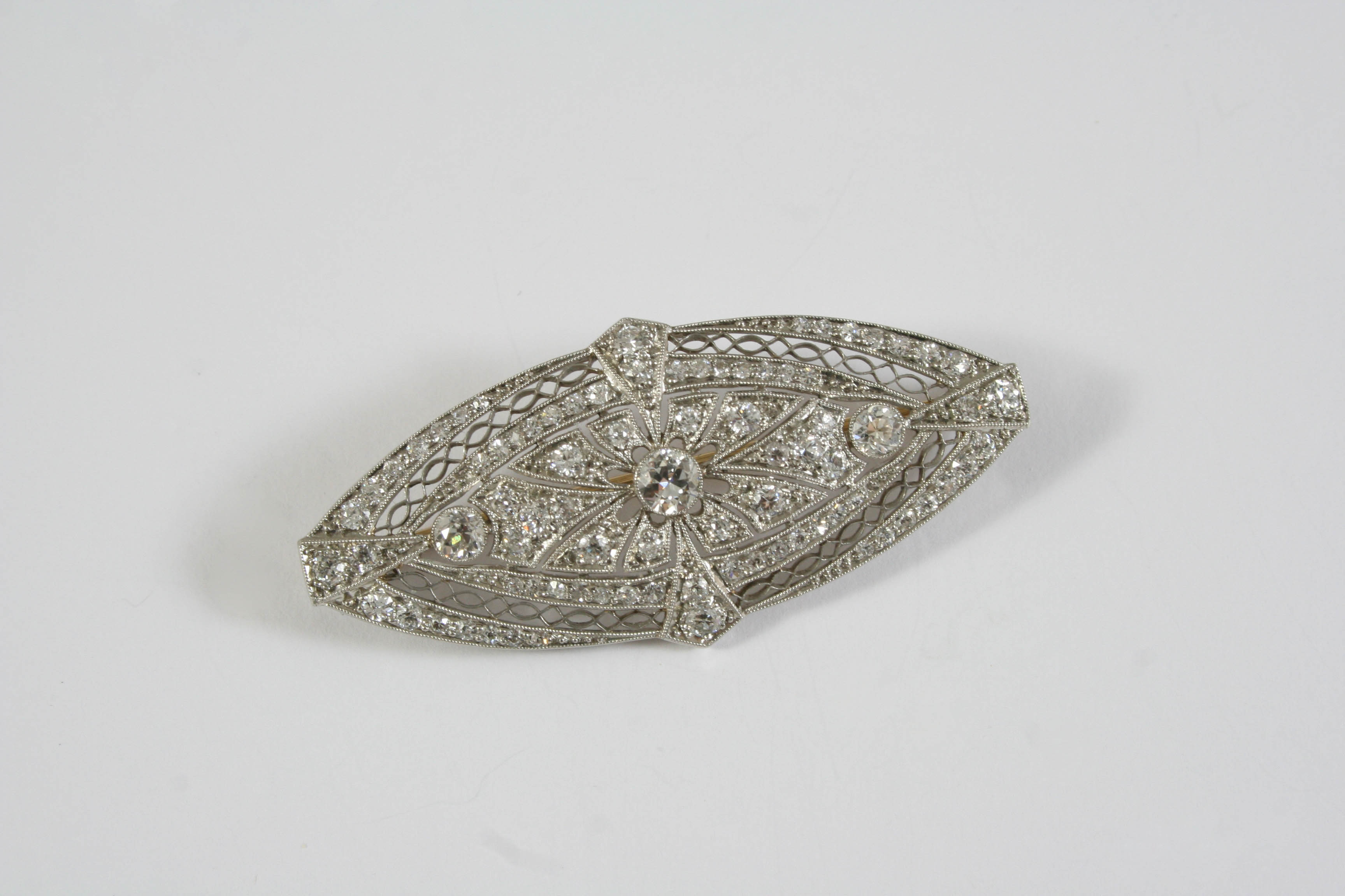 AN EDWARDIAN DIAMOND PLAQUE BROOCH the oval-shaped openwork design is set with three collet set