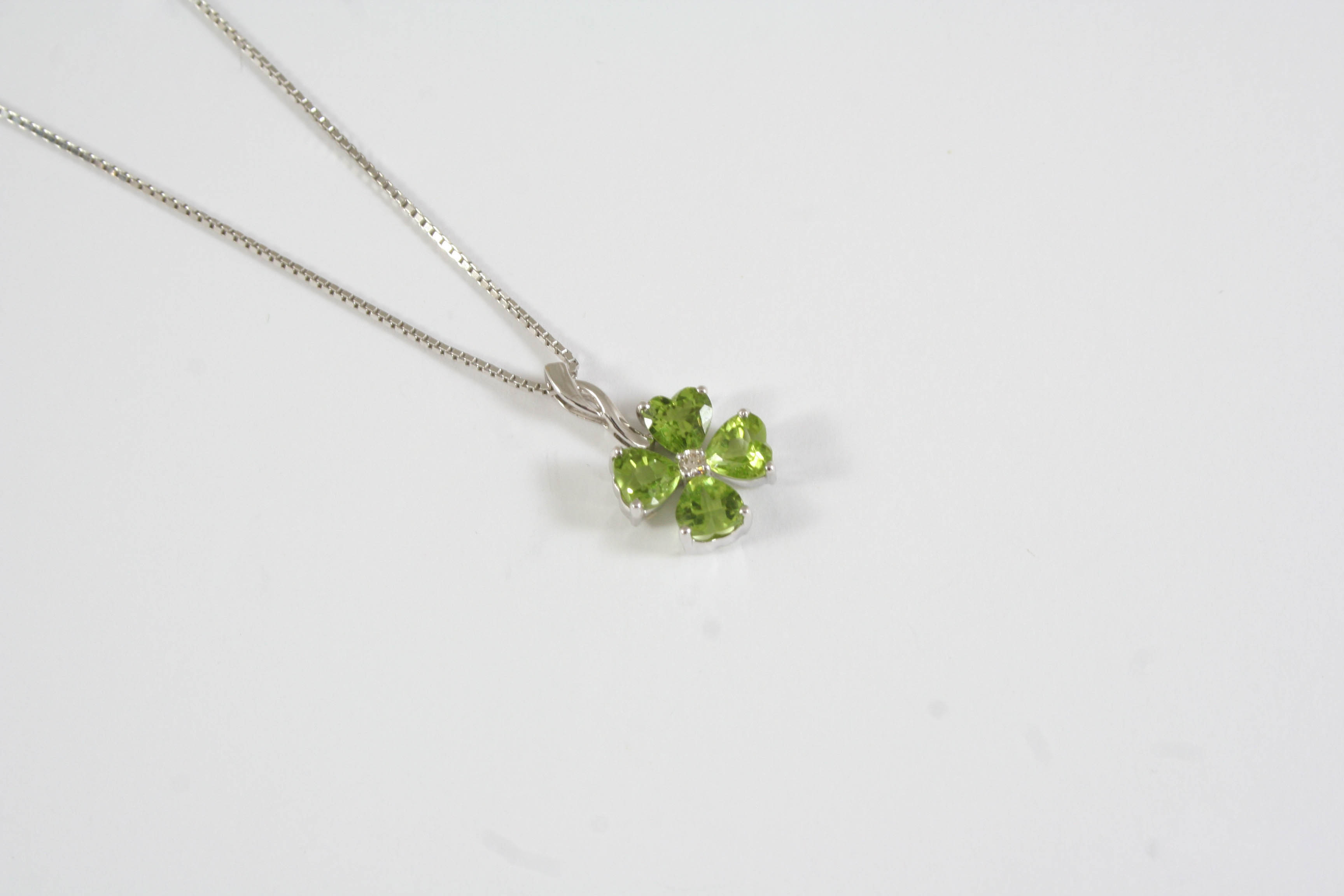 A PERIDOT AND DIAMOND PENDANT the flowerhead design is set with four heart-shaped peridots and a