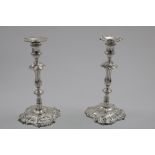 A PAIR OF GEORGE II CAST CANDLESTICKS on shaped square bases, decorated with jusks and scrolls,