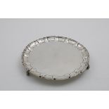 AN EDWARDIAN SALVER of shaped circular outline with a moulded border and scroll feet, crested, by