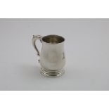 AN EARLY GEORGE III MUG of baluster form with a spreading foot and a leaf-capped scroll handle,
