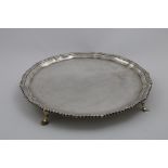 AN EARLY 20TH CENTURY SALVER of shaped circular outline with a gadrooned border and hoof feet, by