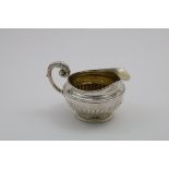 A GEORGE III CREAM JUG with a part-fluted circular body and a leaf wrapped, scroll handle,