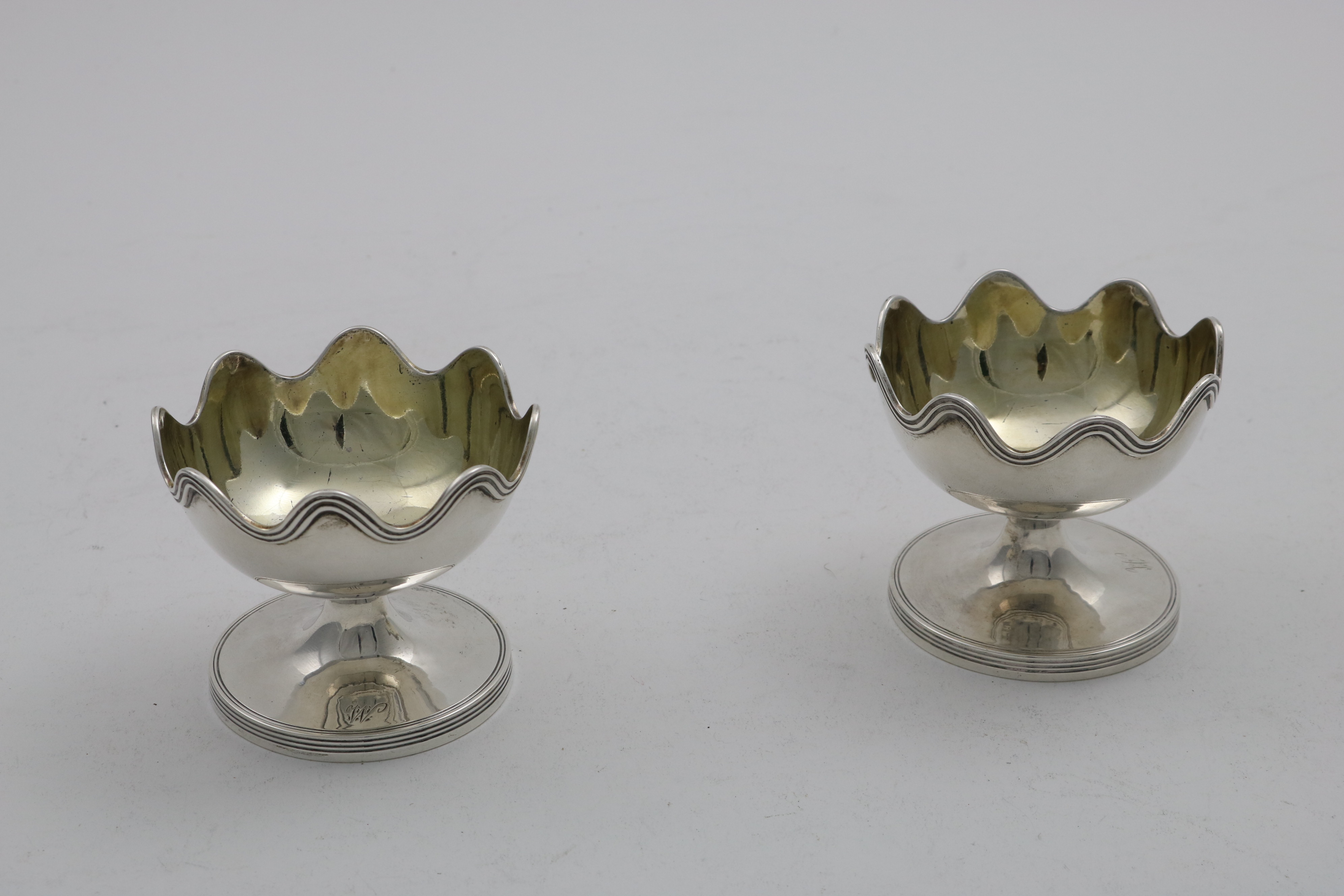 A PAIR OF GEORGE III CIRCULAR SALTS on pedestal bases with reeded borders & wavy rims, gilt
