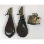 TWO LEATHER AND BRASS SHOT FLASKS AND AN EASTERN FLINT STRIKER. Two similar brass and leather shot