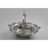 A GEORGE III ROCOCO REVIVAL CAKE BASKET of shaped oval outline with a cast border of scrolls