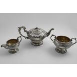 A GEORGE III THREE-PIECE CIRCULAR TEA SET with repousse-work decoration and a vacant cartouche on