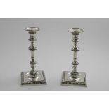 A PAIR OF LATE GEORGE II CANDLESTICKS on square bases with well centres, knopped and shouldered,