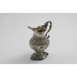 A GEORGE II EMBOSSED CREAM JUG on a cast rocaille foot with a cast serpent & scroll handle, a shaped