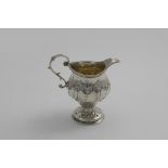 AN EARLY GEORGE III CREAM JUG on a circular pedestal foot, decorated with wrythen embossing and a