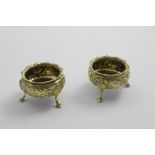 A PAIR OF EARLY VICTORIAN SILVERGILT SALTS on three legs with repousse-work decoration, engraved