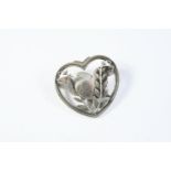 A SILVER BROOCH BY GEORG JENSEN depicting a bird amongst foliage, in a heart surround, with maker'