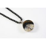 A WHITBY JET BEAD NECKLACE on a circular silver pendant mounted to one side with a Blue John