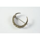 A SILVER AND PASTE SET CLOSED CRESCENT BROOCH mounted with graduated circular white paste stones,