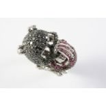 A RUBY AND DIAMOND NOVELTY DRESS RING in the form of a skull with a hand covering the mouth, set