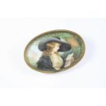 A PORTRAIT MINIATURE BROOCH depicting a young girl in a large hat reading a book under a tree, in