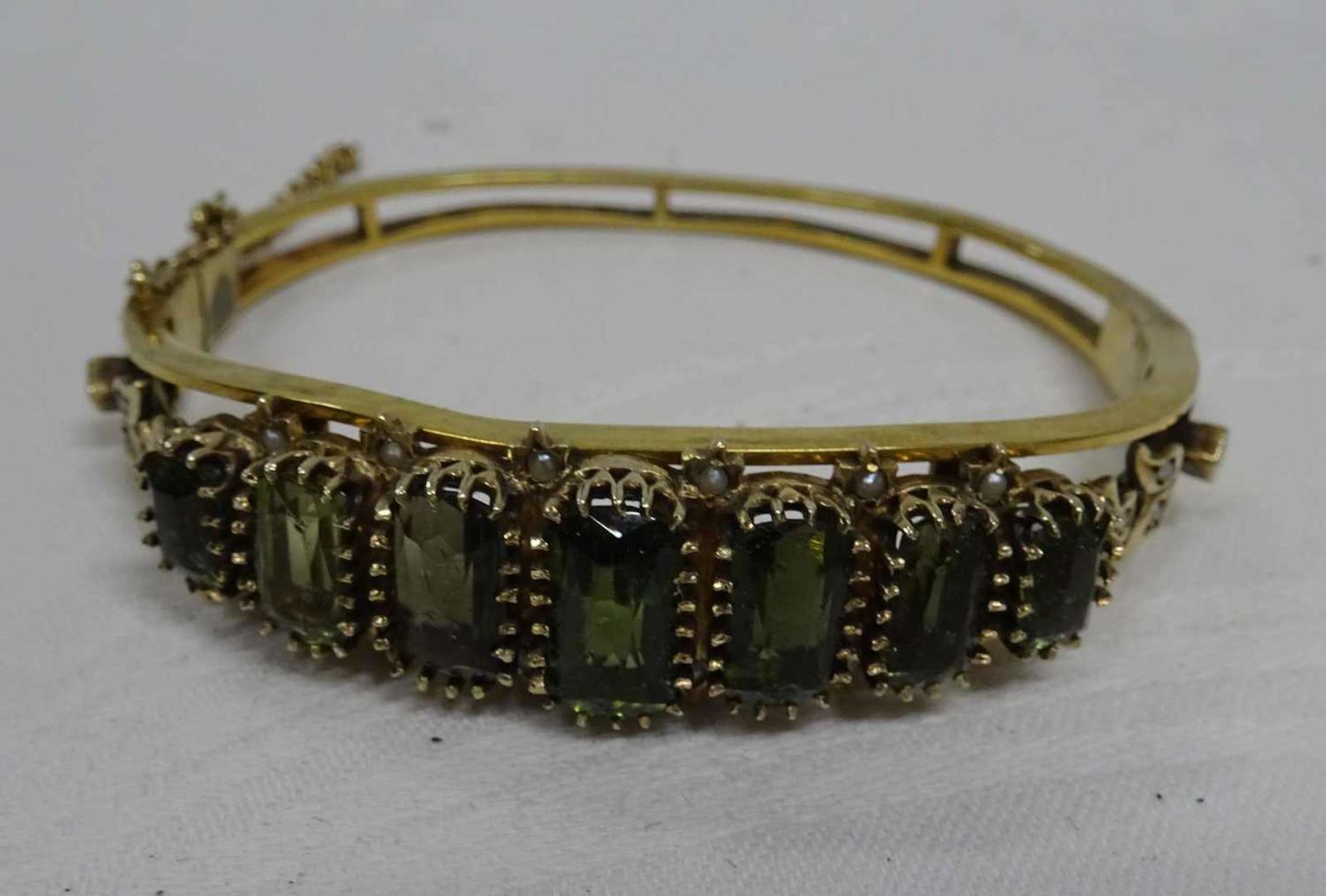 Bangle, gold-plated silver. Set with green glass stones. Diameter approx. 6 cm. With safety chain.