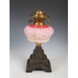 A Victorian cast iron and gilt metal mounted oil lamp, with opaque pink glass reservoir, on