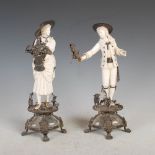 A pair of late 19th century white metal mounted ivory figure groups, modelled with lady holding a