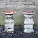 A pair of late 19th century fire clay garden urns, of campagna form, on square plinth bases with