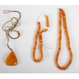 An amber pendant and two amber necklaces, the pendant of shaped triangular form, 15.2 grams, the