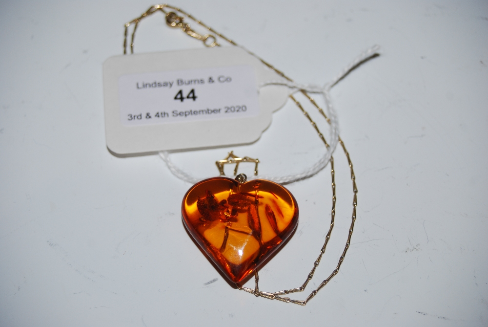 A 9CT GOLD CHAIN SUSPENDING HEART SHAPED AMBER PENDANT