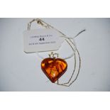 A 9CT GOLD CHAIN SUSPENDING HEART SHAPED AMBER PENDANT