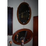 AN OAK FRAMED OVAL BEVELLED WALL MIRROR TOGETHER WITH MAHOGANY FRAMED OVAL BEVELLED WALL MIRROR