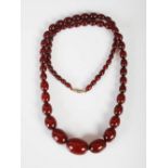 A red amber bead necklace, formed from sixty five graduated oval beads, 60.4 grams.