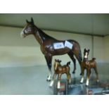 A bay Beswick horse together with two Beswick foals
