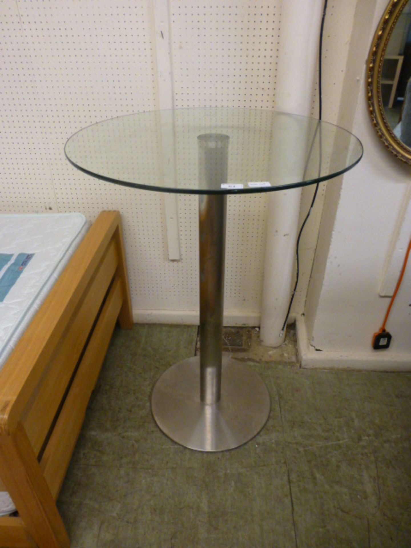 A circular glass topped table on chromed base