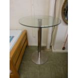 A circular glass topped table on chromed base