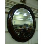 An early 20th century mahogany cushion moulded oval beveled glass mirror