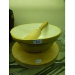 A ceramic mixing bowl together with a circular wooden chopping board and a wooden pestle