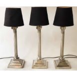 TABLE LAMPS, a set of three, silvered with Corinthian capped reeded columns and stepped bases,