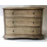 COMMODE, Continental style limed oak of serpentine outline with three long drawers and bun supports,