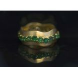 AN EIGHTEEN CARAT GOLD AND EMERALD BAND RING, set with a wavy band of circular cut emeralds to the