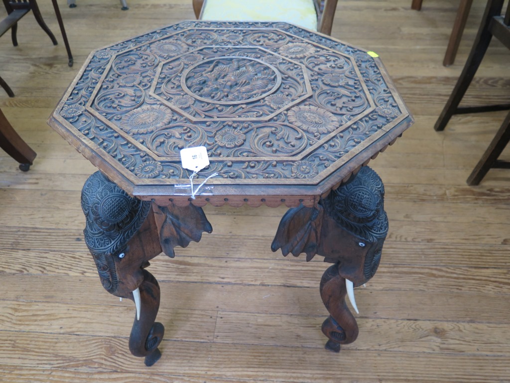 An Indian carved wood octagonal table, the heavily carved top depicting three figures, on a