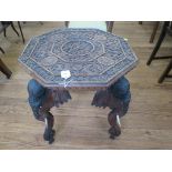 An Indian carved wood octagonal table, the heavily carved top depicting three figures, on a