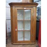 A pine hanging corner cabinet, the dentil cornice over a glazed door enclosing two shaped shelves,