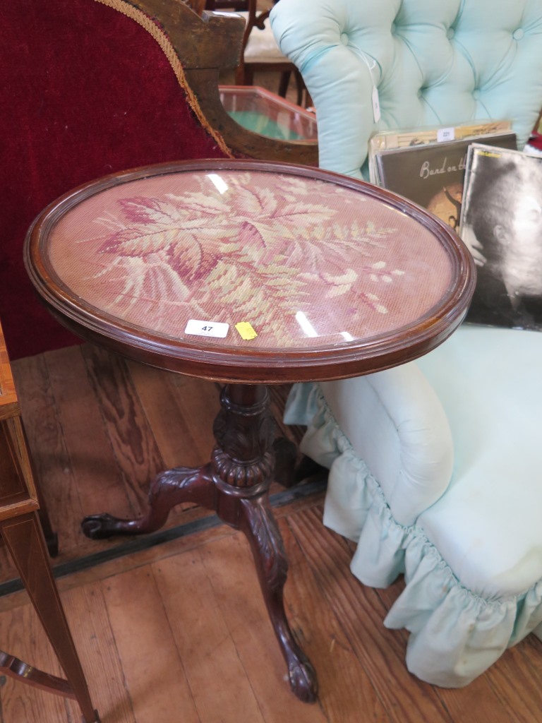 A George III style tripod table, the oval top with foliate woolwork panel, over an acanthus carved