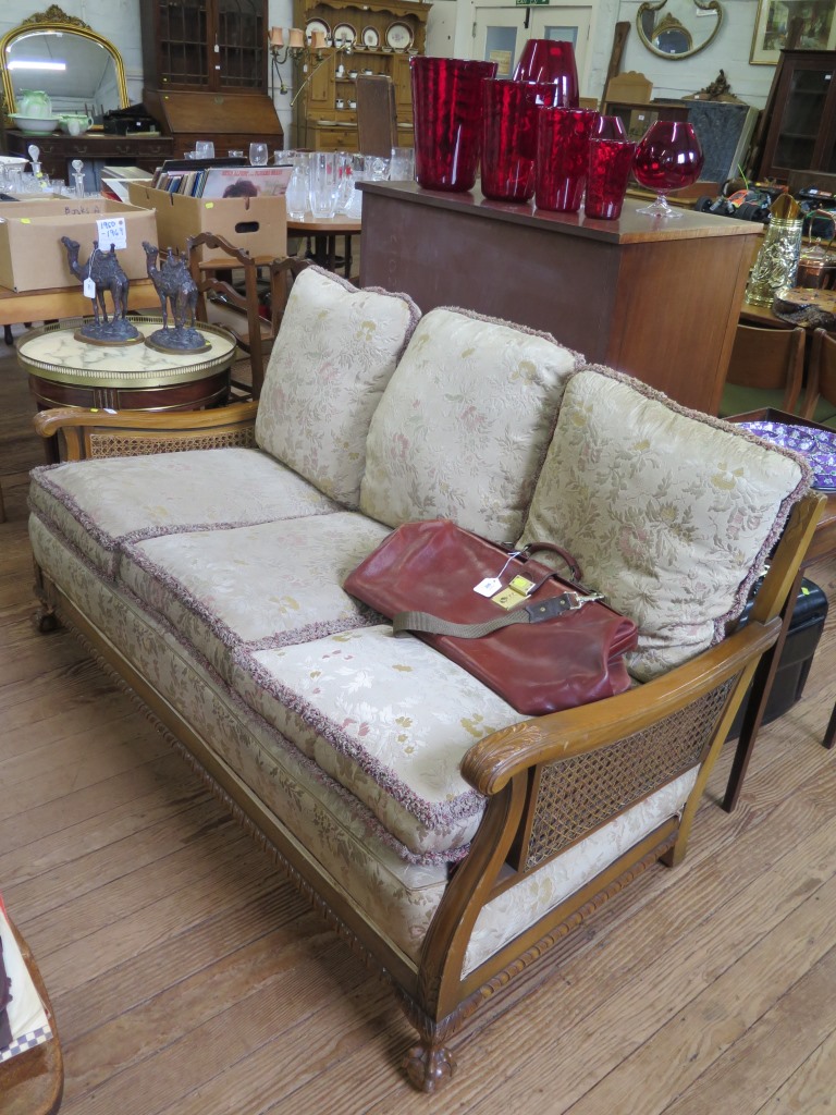 A 1930s walnut bergere settee, with cane back and double caned scroll arms, on acanthus carved