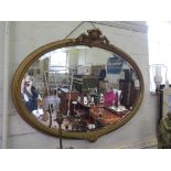 A giltwood oval wall mirror, the beaded frame with cabochon and foliate mounts, enclosing a bevelled